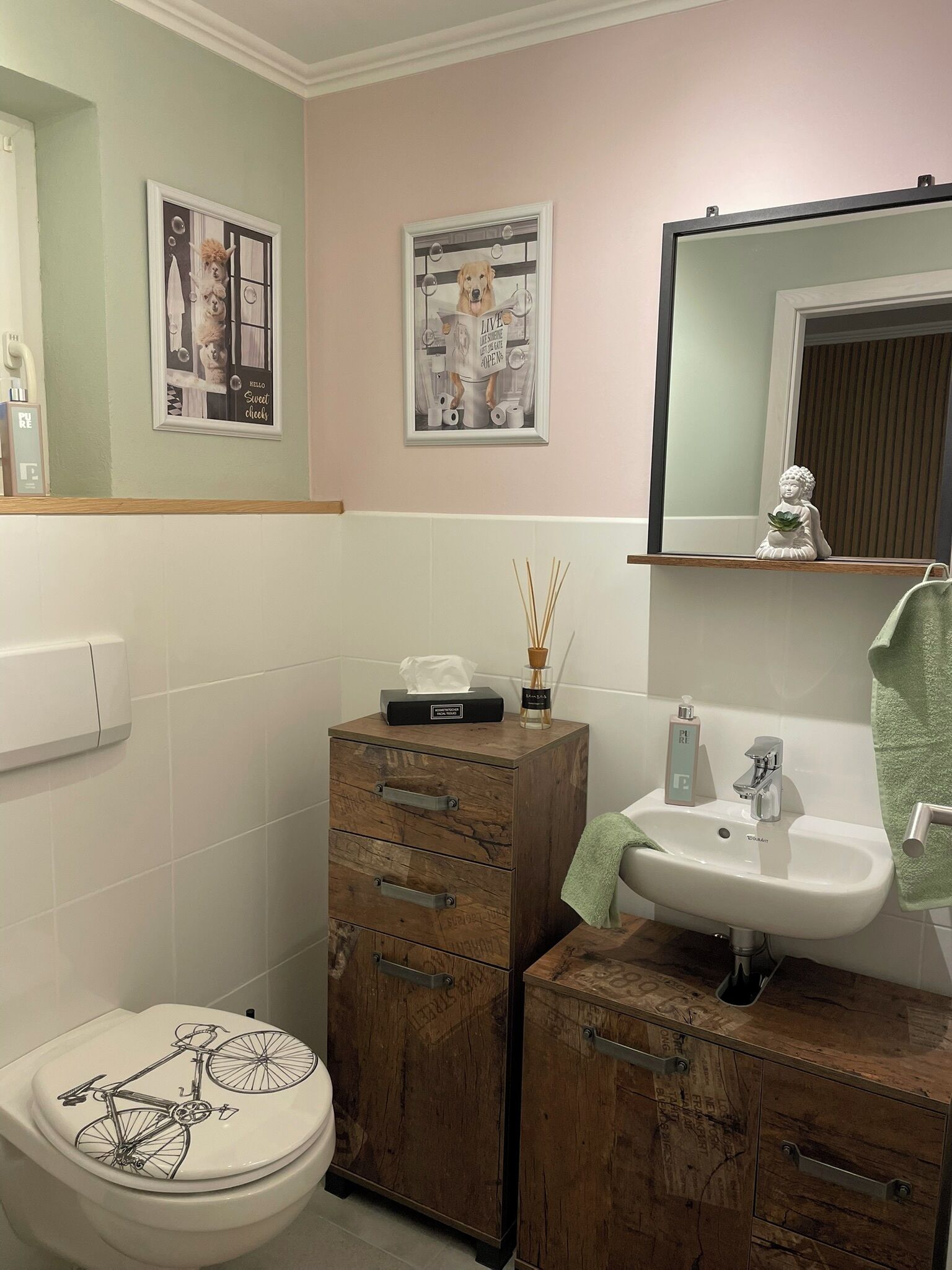 Une salle de bain comprenant des toilettes, un meuble en bois, un lavabo et deux tableaux encadrés accrochés au mur.