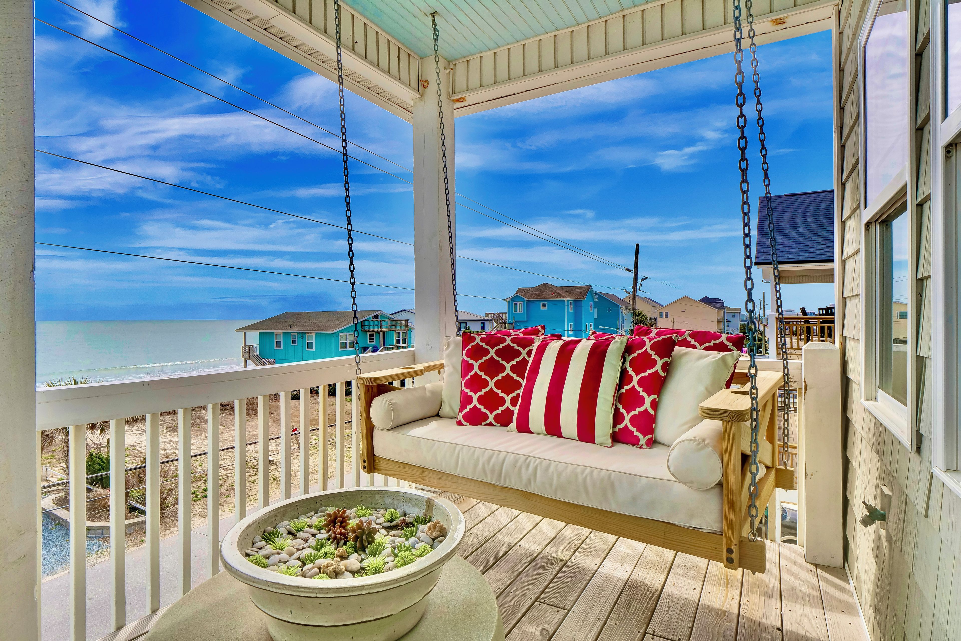 A porch with a swing chair, a bowl of decorative stones, and a view of the ocean and houses.