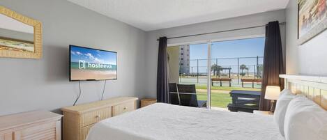 Habitación de hotel con cama, televisor, cómoda de mimbre y vistas al exterior.
