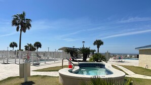 Zona de piscina con jacuzzi, palmeras y sillones de descanso.
