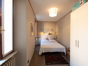 Un dormitorio con cama, lámparas de noche, mesita de noche, ventana y radiador.