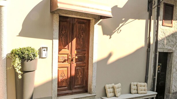 A stone bench with cushions, a wooden door with intricate carvings, and a planter with greenery. - Lovely apartment for 3 guests with WIFI, TV and balcony (Mergozzo)