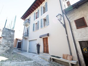 Un edificio de dos pisos con base de piedra, puerta de garaje gris y puerta de madera.