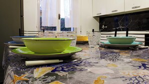 Een keuken met witte kasten, een zwart marmeren achterwand en een tafelkleed met een patroon.