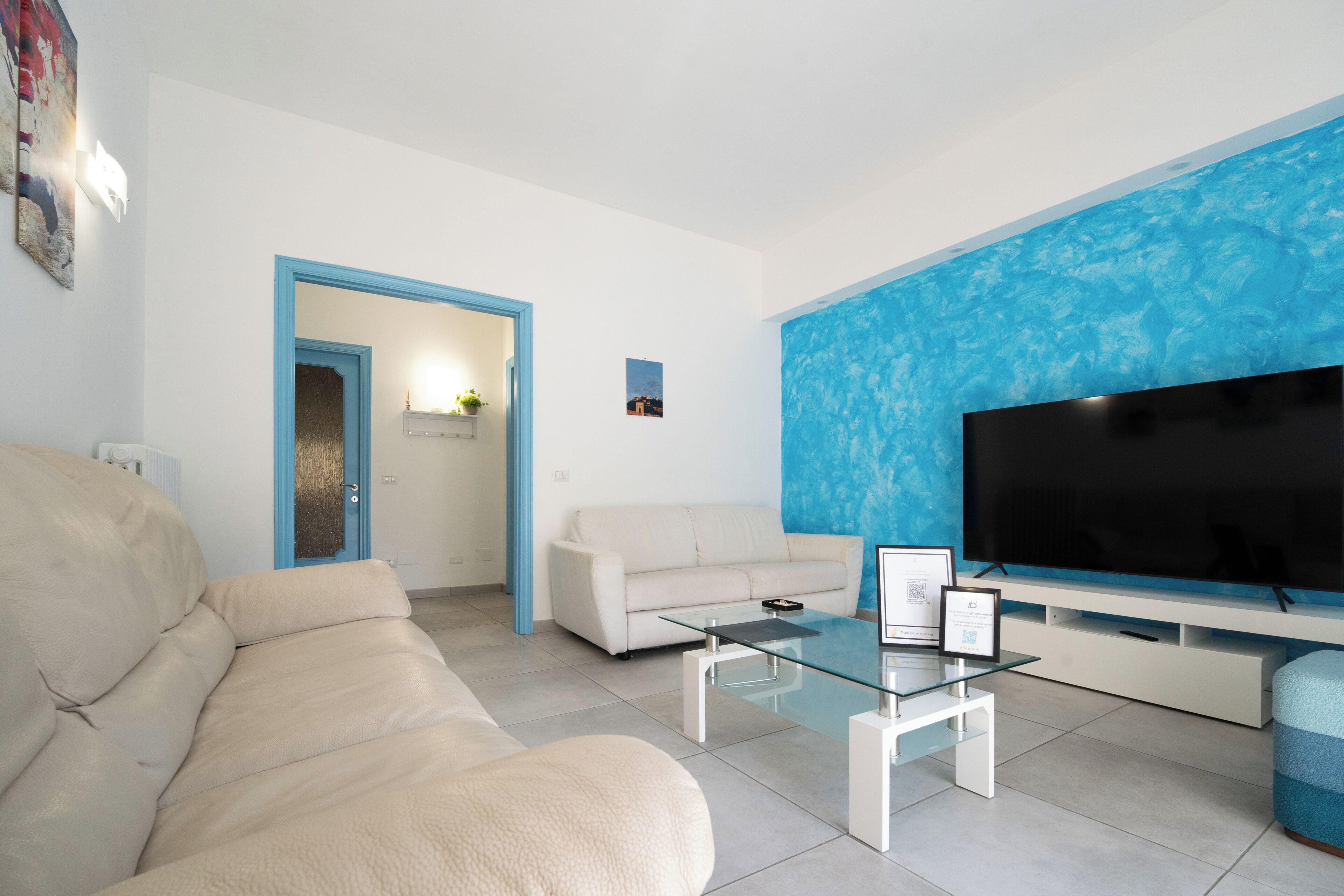 Een woonkamer met een beige bank, een glazen salontafel, een flatscreen televisie en een blauwe accentmuur.