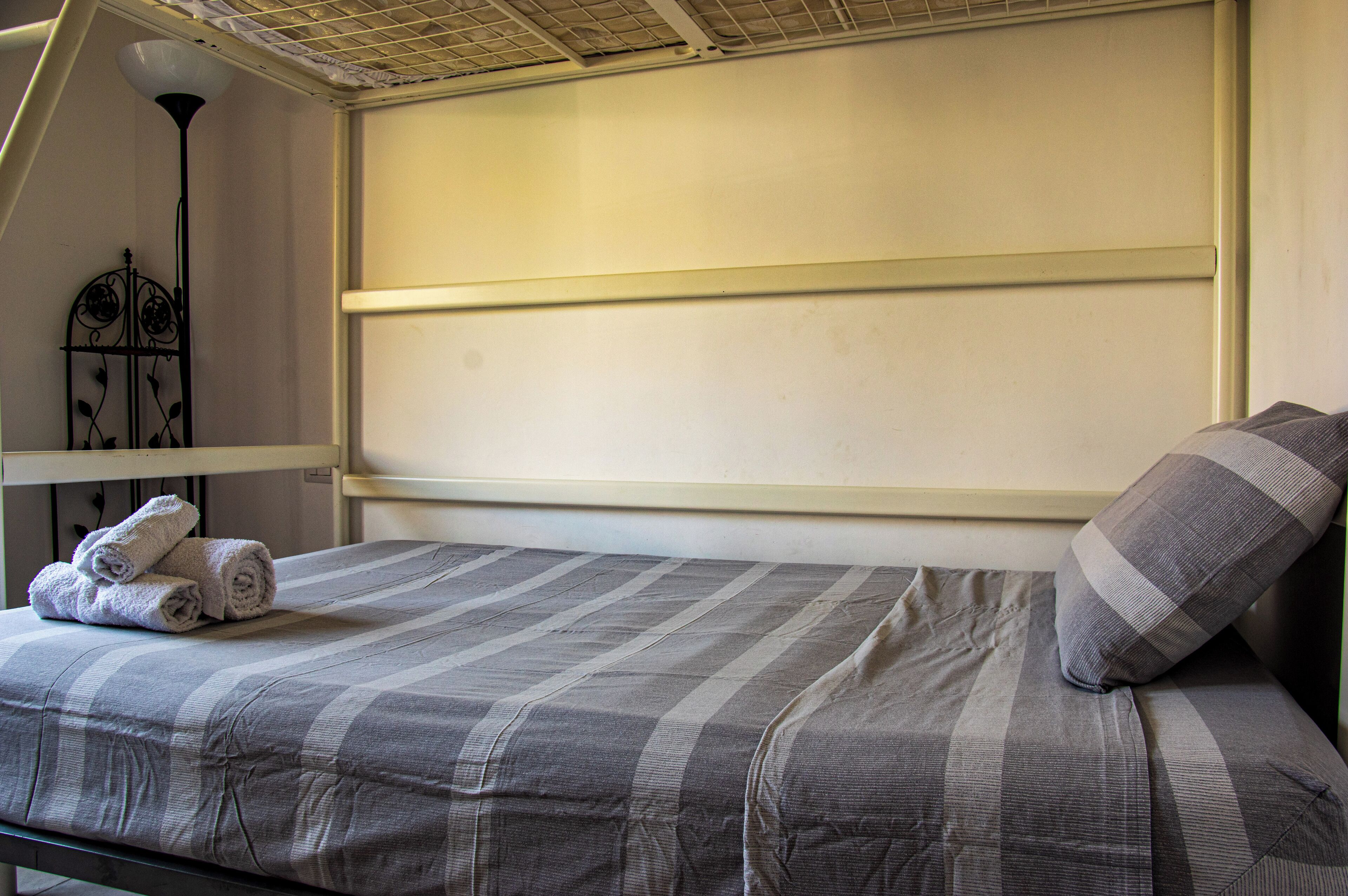 A single bed with a striped bedspread, a rolled towel on the bed, and a pillow on the right side.