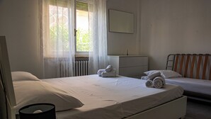 Een slaapkamer met twee bedden, een radiator, een nachtkastje en een raam met dunne gordijnen.