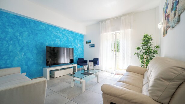 Een moderne woonkamer met een flatscreen televisie, twee blauwe fauteuils, een glazen salontafel en een beige bank.