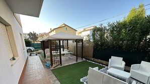 Een terras met een pergola, tuinmeubilair en een stukje gazon.
