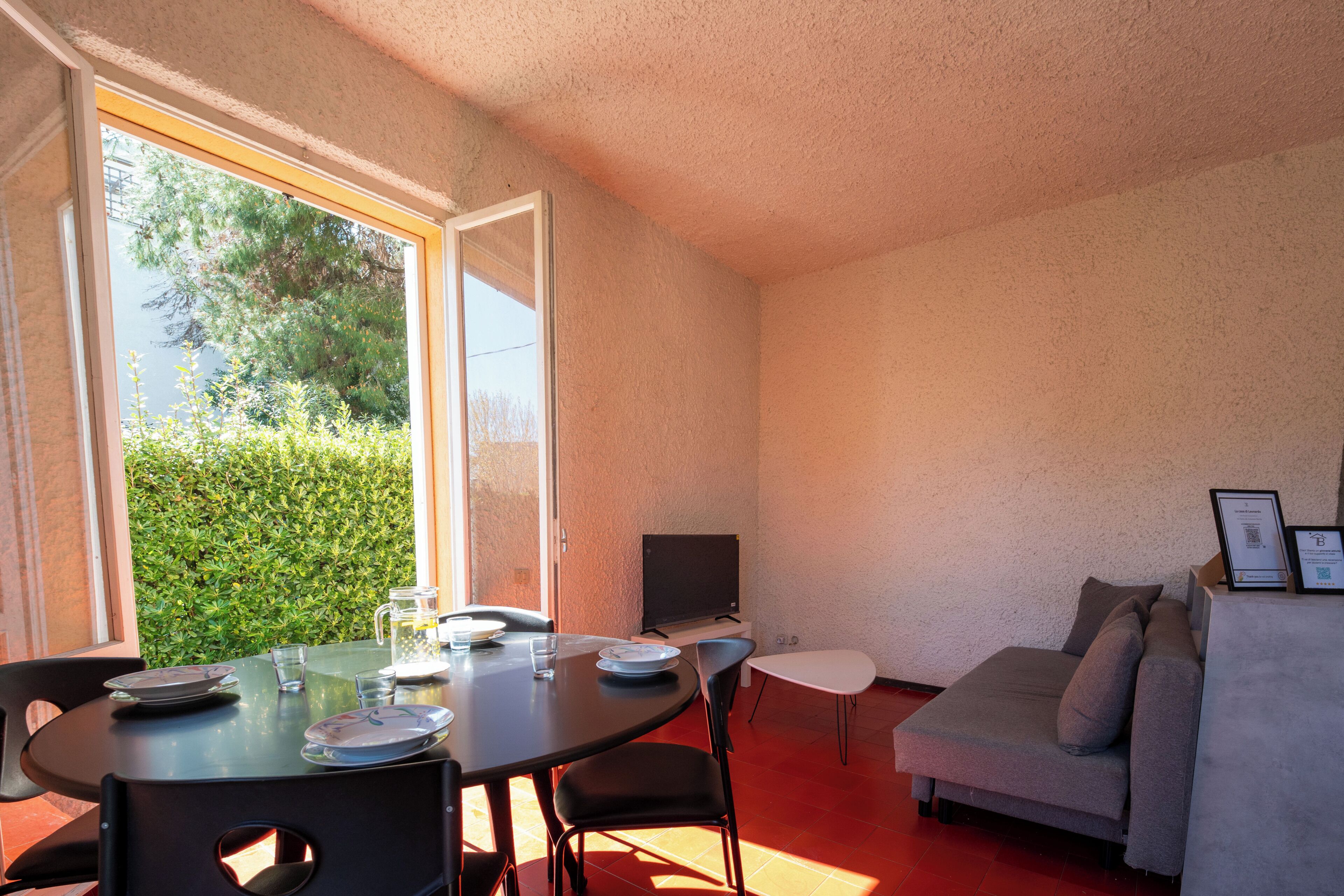 Une pièce comprenant une table à manger, des chaises, un canapé, un téléviseur et une fenêtre donnant sur un paysage verdoyant.