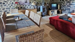 Un salon chaleureux avec un mur en pierre, des poutres apparentes en bois au plafond, une cheminée, un téléviseur et un canapé rouge.