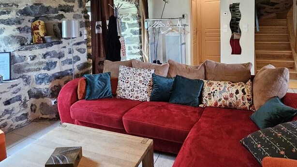 Un salon chaleureux avec un canapé d’angle rouge, une table basse en bois et un mur en pierre.