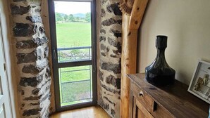 Une pièce avec un mur en pierre, des poutres en bois, une armoire en bois et une porte donnant sur un espace extérieur verdoyant.