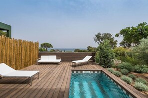 Eine Holzterrasse mit Schwimmbad, zwei Liegestühlen und Meerblick.