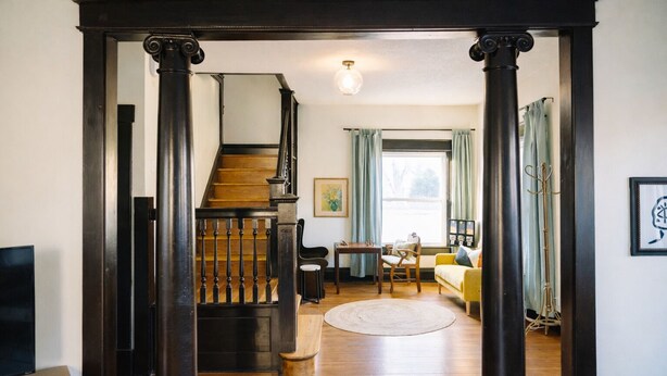 Una escalera conduce a una sala de estar con un sofá, una mesa y un ventanal con cortinas.