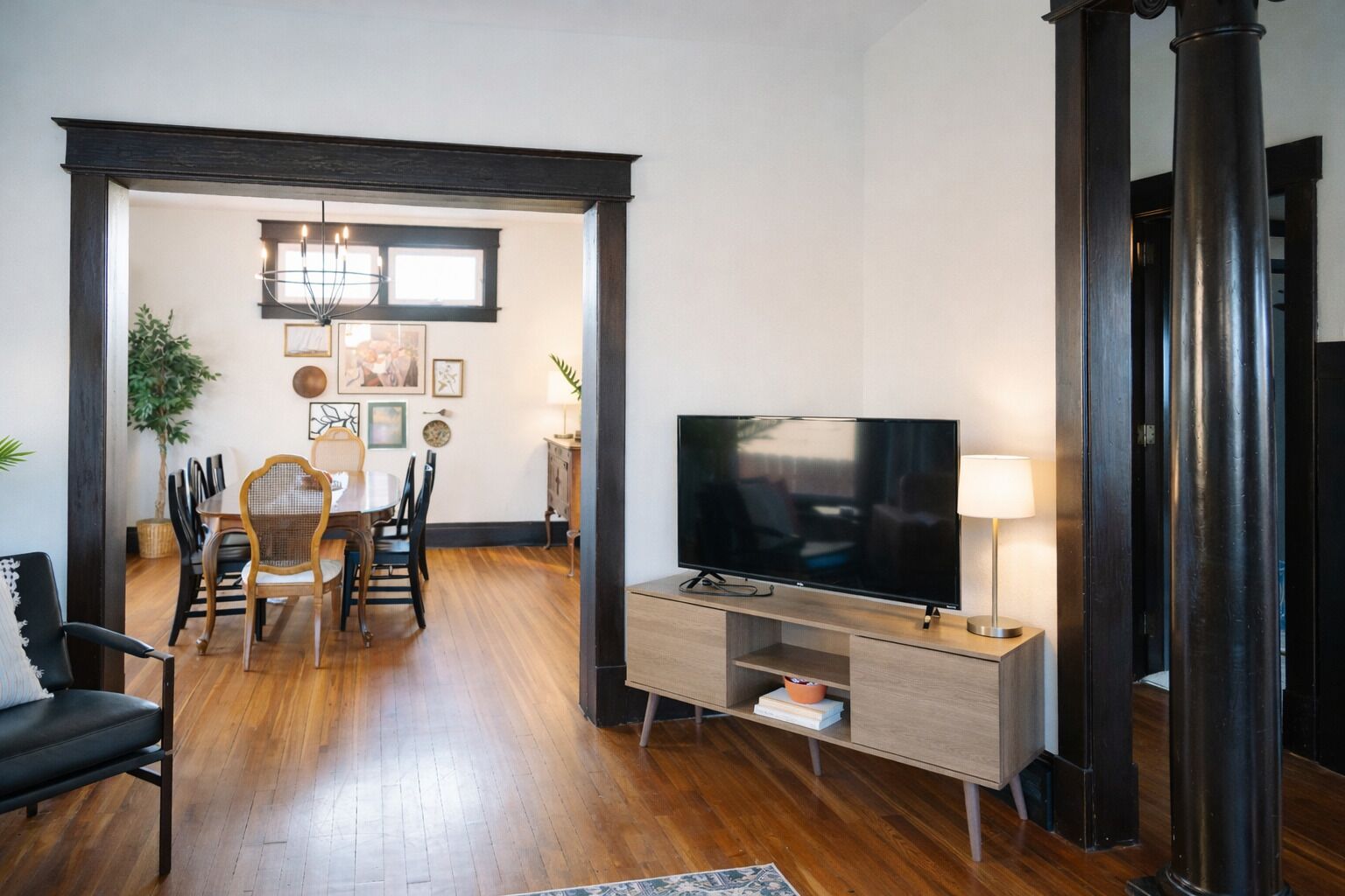 A modern living room with a flat-screen TV, a dining area with chairs and a table, and a large plant.