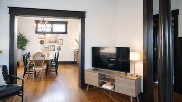 A modern living room with a flat-screen TV, a dining area with chairs and a table, and a large plant.