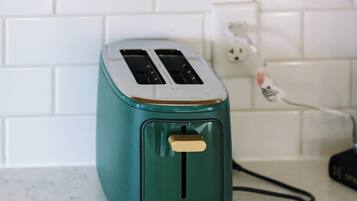 Een blauwgroene toaster op een wit aanrecht met een witte betegelde achterwand en een goudkleurige hendel erboven.