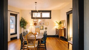 Un comedor con mesa de madera, sillas, una araña y obras de arte en las paredes.