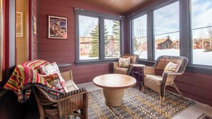 A cozy room with wicker furniture, a patterned rug, and large windows offering a view of the outside. - Teton Homestead: Teton Basecamp Near Parks (Driggs)