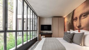 Une chambre à coucher moderne, dotée d’un grand lit, d’une télévision et d’une fresque représentant une œuvre célèbre sur le mur.