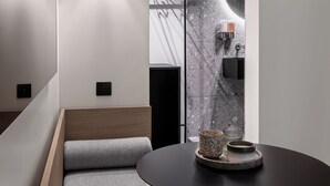 Une chambre d’hôtel moderne au design minimaliste, comprenant un canapé, une table ronde et un miroir fixé au mur.