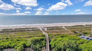 Un paysage côtier avec une plage, une route menant à un parking et une végétation luxuriante au premier plan.