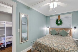Un dormitorio con una cama litera, un espejo grande, un ventilador de techo y un adorno decorativo en la ventana.
