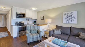 Un espace de vie compact comprenant un coin cuisine, un fauteuil à rayures grises, un canapé gris et un panneau décoratif accroché au mur.