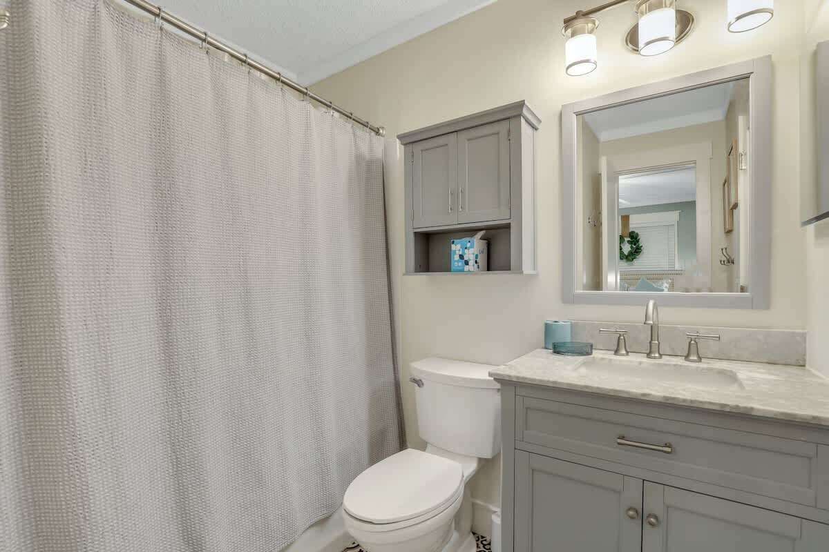 A bathroom with a shower curtain, toilet, vanity with a mirror, and a sink.
