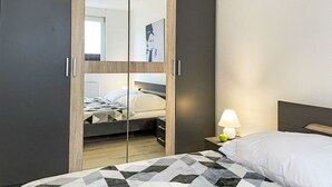 Quarto com cama, mesa de cabeceira com abajur e guarda-roupa com espelho.