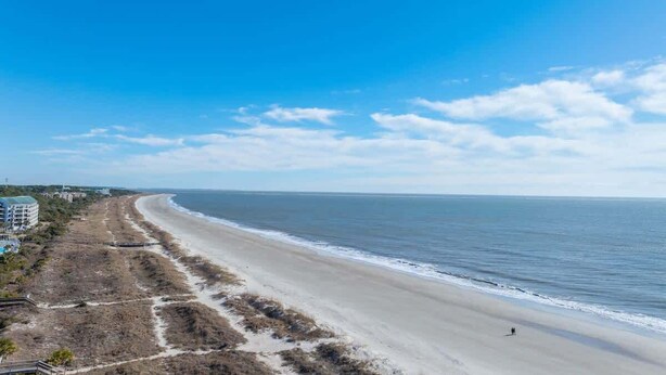A beach with a clear view of the ocean and a few buildings in the background. - Tennis Villa C14 - Easy Walk to the Beach! (Hilton Head Island)