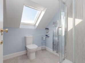 Un baño moderno con tragaluz, inodoro, toallero y mampara de cristal.