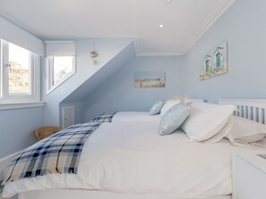 Un dormitorio con cama, dos ventanas, techo inclinado y lámpara fijada a la pared.