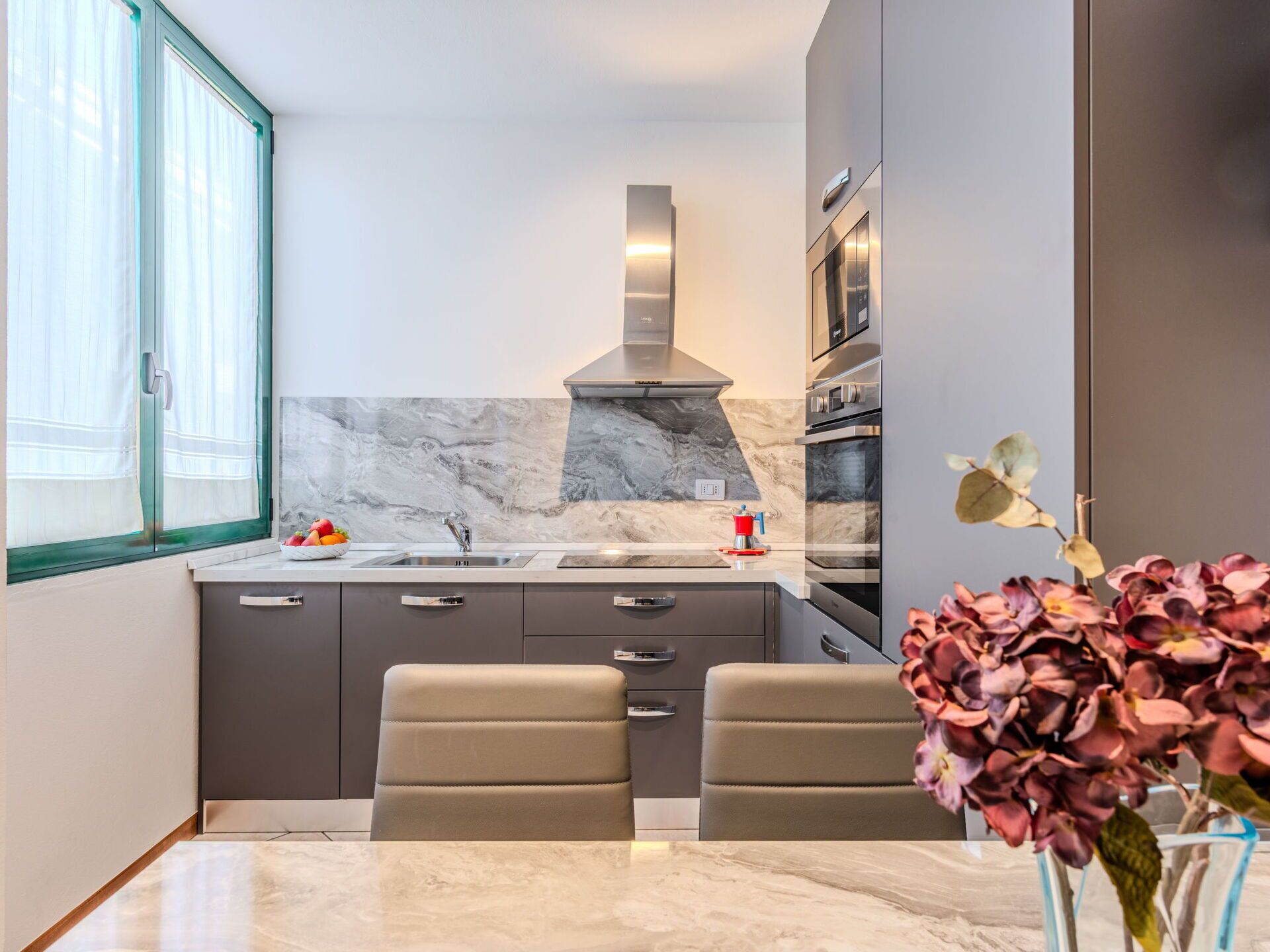 A modern kitchen with a marble backsplash, stainless steel appliances, and a dining area with two chairs.