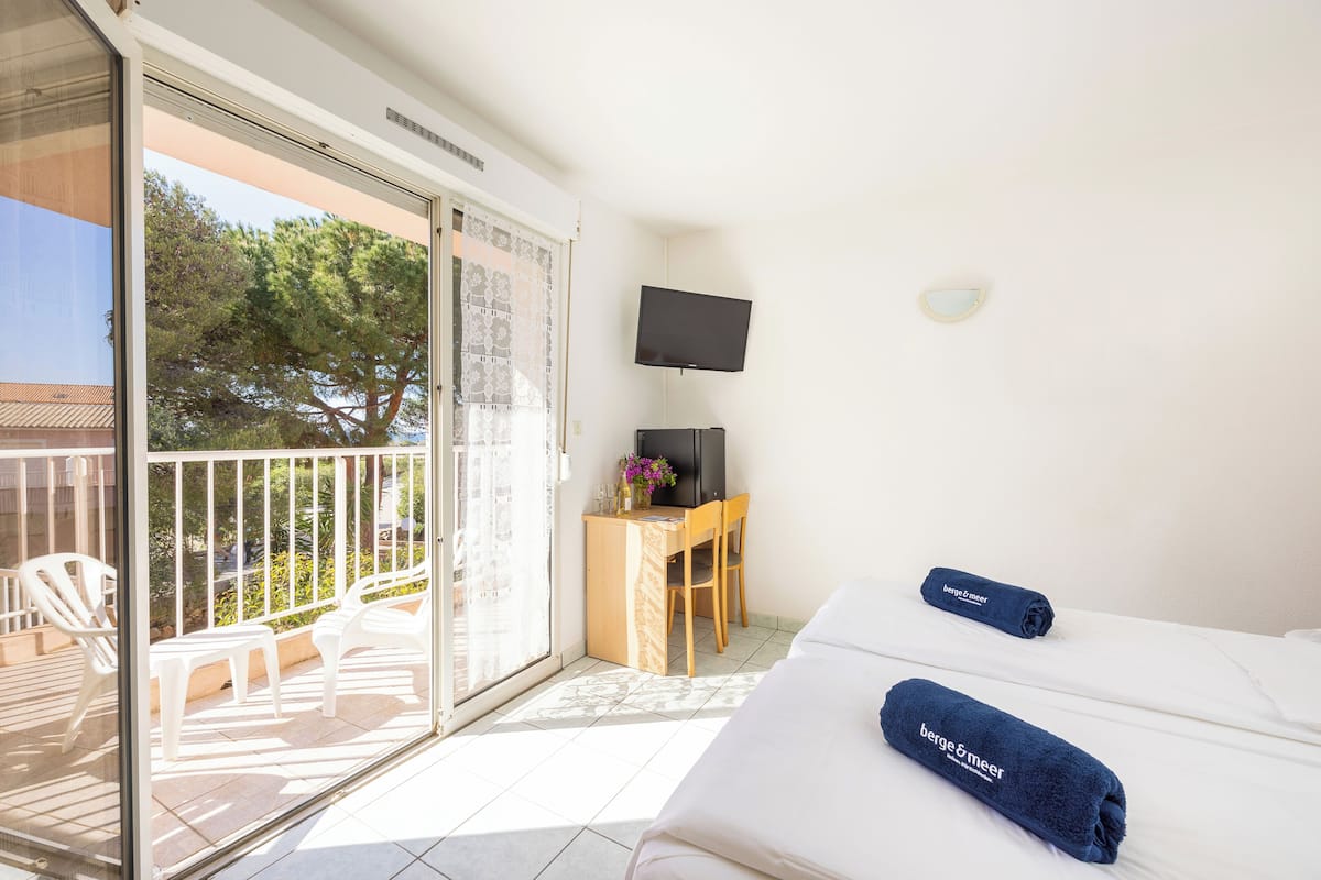 Une chambre d’hôtel avec un balcon, un bureau avec une chaise, un téléviseur à écran plat et deux lits avec des serviettes bleues.