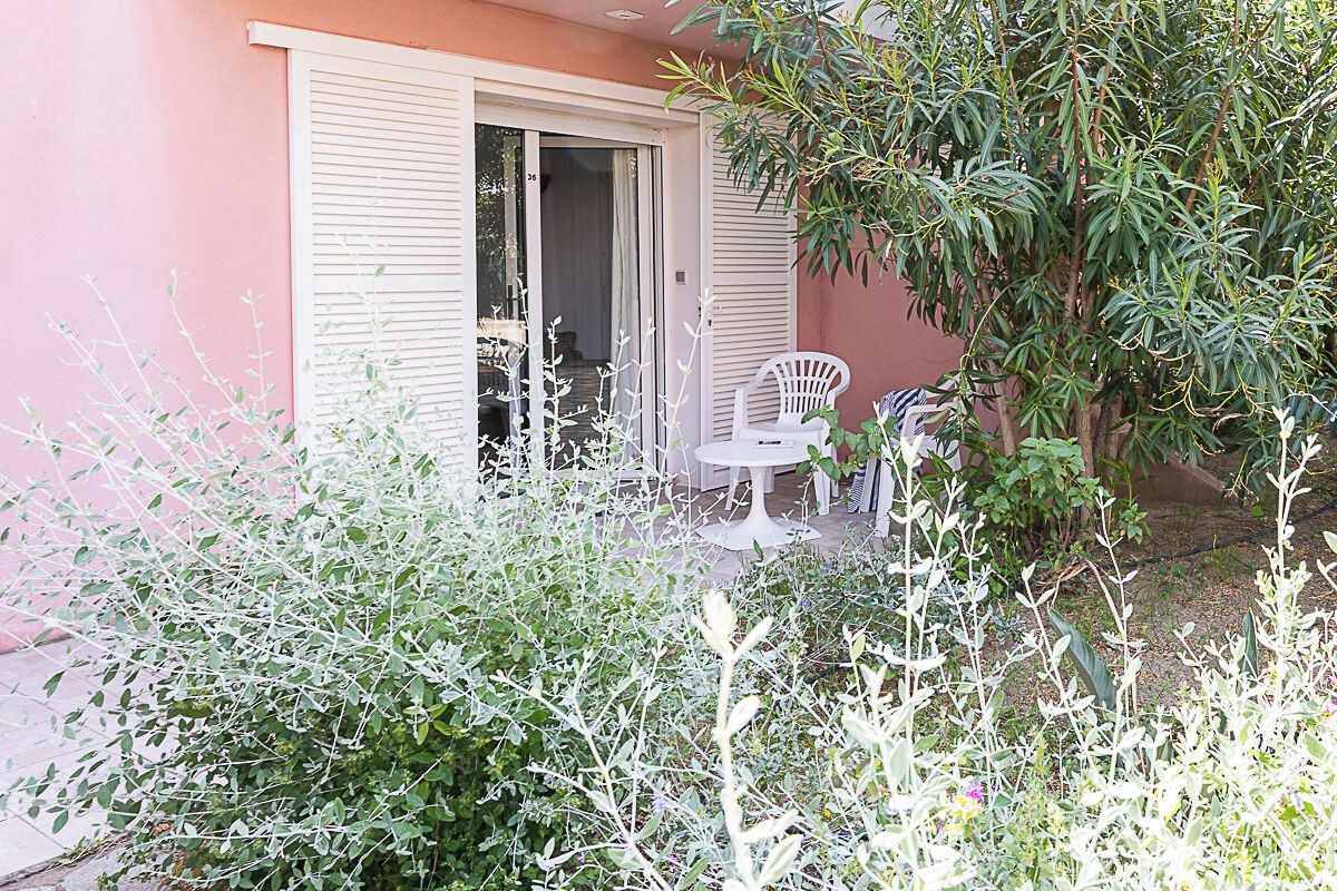 Un espace patio avec une chaise et une table blanches, une porte-fenêtre coulissante et un jardin avec différentes plantes.
