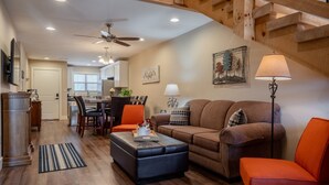 A spacious living area with a sofa, ottoman, and a dining table with chairs. A ceiling fan and a lamp are visible. - Rustic Wooded Branson Retreat Near Lake Taneycomo | RH230B (Branson)