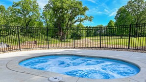 A hot tub surrounded by a black metal fence, set against a backdrop of trees and a clear sky. - Rustic Wooded Branson Retreat Near Lake Taneycomo | RH230B (Branson)