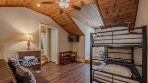 A cozy loft bedroom with a bunk bed, a sofa, a lamp, and a TV. - Rustic Wooded Branson Retreat Near Lake Taneycomo | RH230B (Branson)