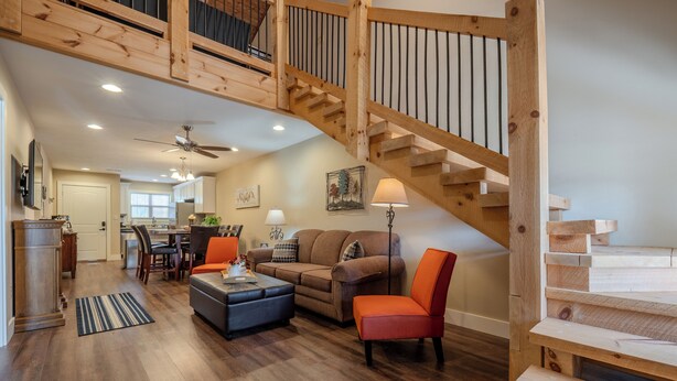 A spacious living area with a wooden staircase, a sofa, a coffee table, and a lamp. - Rustic Wooded Branson Retreat Near Lake Taneycomo | RH230B (Branson)