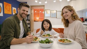 Une famille est assise autour d’une table ronde, recouverte d’une nappe blanche, et prend son repas.