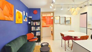 Un salon moderne avec un mur bleu, un canapé vert, une table à manger avec des chaises et une bibliothèque.