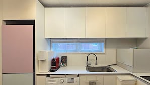 Une cuisine compacte équipée d’un lave-linge, d’un évier et d’une fenêtre située au-dessus du plan de travail.