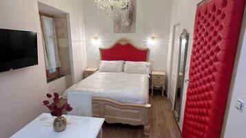 Un dormitorio con cama, televisor, candelabro, espejo y puerta roja.