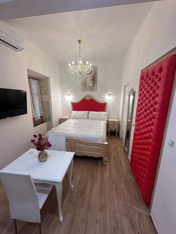 A bedroom with a bed, a TV, a chandelier, a mirror, and a red door. - Small studio Presbytery in the Church (Narbonne)