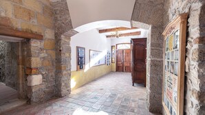 Un pasillo de paredes de piedra con suelo de baldosas, una puerta de madera y un cartel enmarcado en la pared.