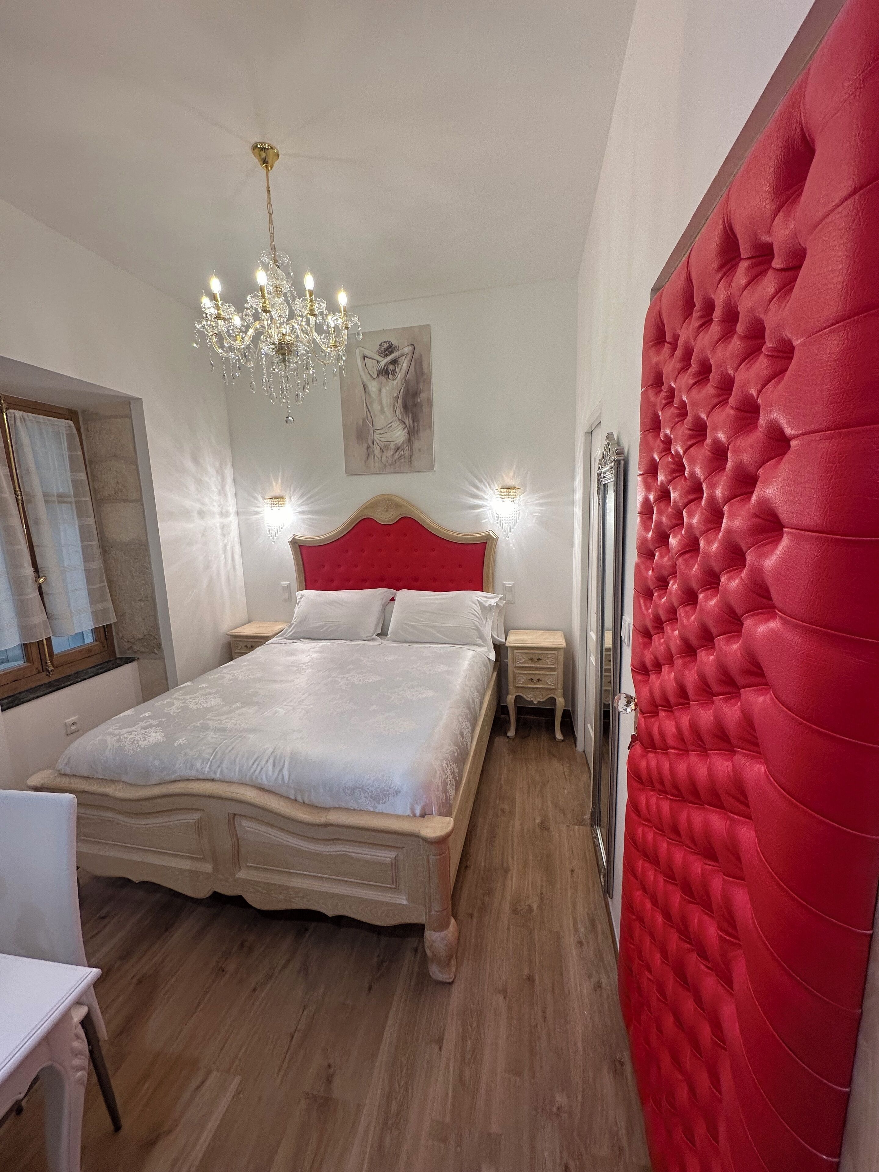 Un dormitorio con una cama grande, una araña, una pared acolchada roja y un cuadro en la pared.