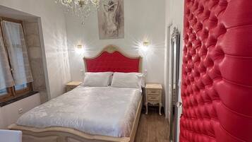 Un dormitorio con una cama grande, una araña, una pared acolchada roja y un cuadro en la pared.