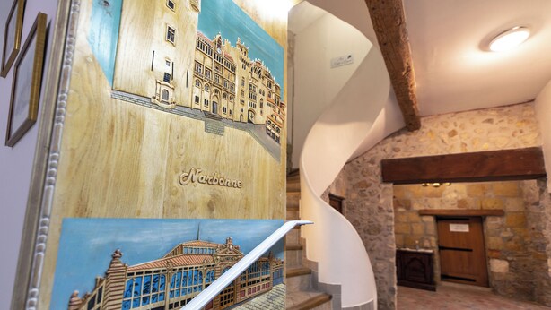 Un panel de madera con una ilustración de un edificio, una escalera con paredes de piedra y una puerta de madera.